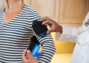 A clinician applies a wearable device to a woman's upper arm as she holds a blue Oska Pulse package